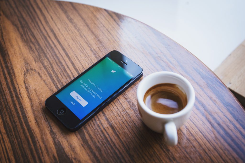 Mobile phone with Twitter sign-in placed on table next to coffee